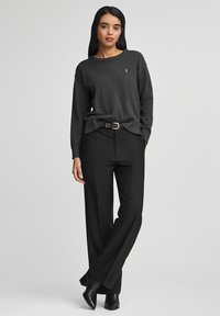 Grauer Pullover mit lockerer Passform und geripptem Kragen, kombiniert mit schwarzen weit geschnittenen Hosen und schwarzen Stiefeletten. Ein einfacher Gürtel als Akzent.