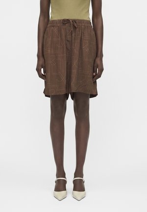 Person iført brune mønstrede shorts med snor, en olivengrøn tanktop og cremefarvede spidse hæle med ankelremme.