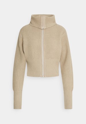 Suéter beige de punto con cremallera, cuello alto, mangas largas y puños y cintura acanalados.