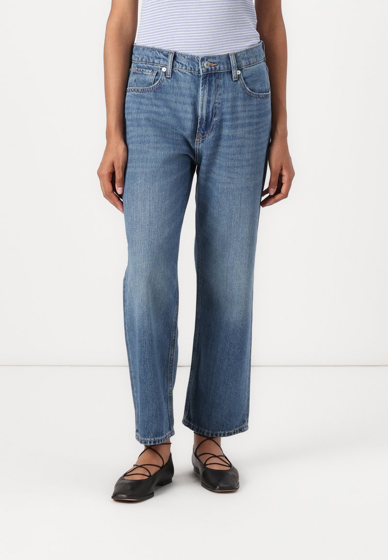 Jeans de denim azul claro com um design de perna reta, cintura média e desbotamento sutil. Combinados com sapatilhas pretas com tiras cruzadas.