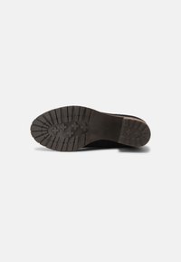 Semelle extérieure en caoutchouc noir avec un motif de crampons profonds, comportant des lignes horizontales et verticales, conçue pour la traction et la durabilité.