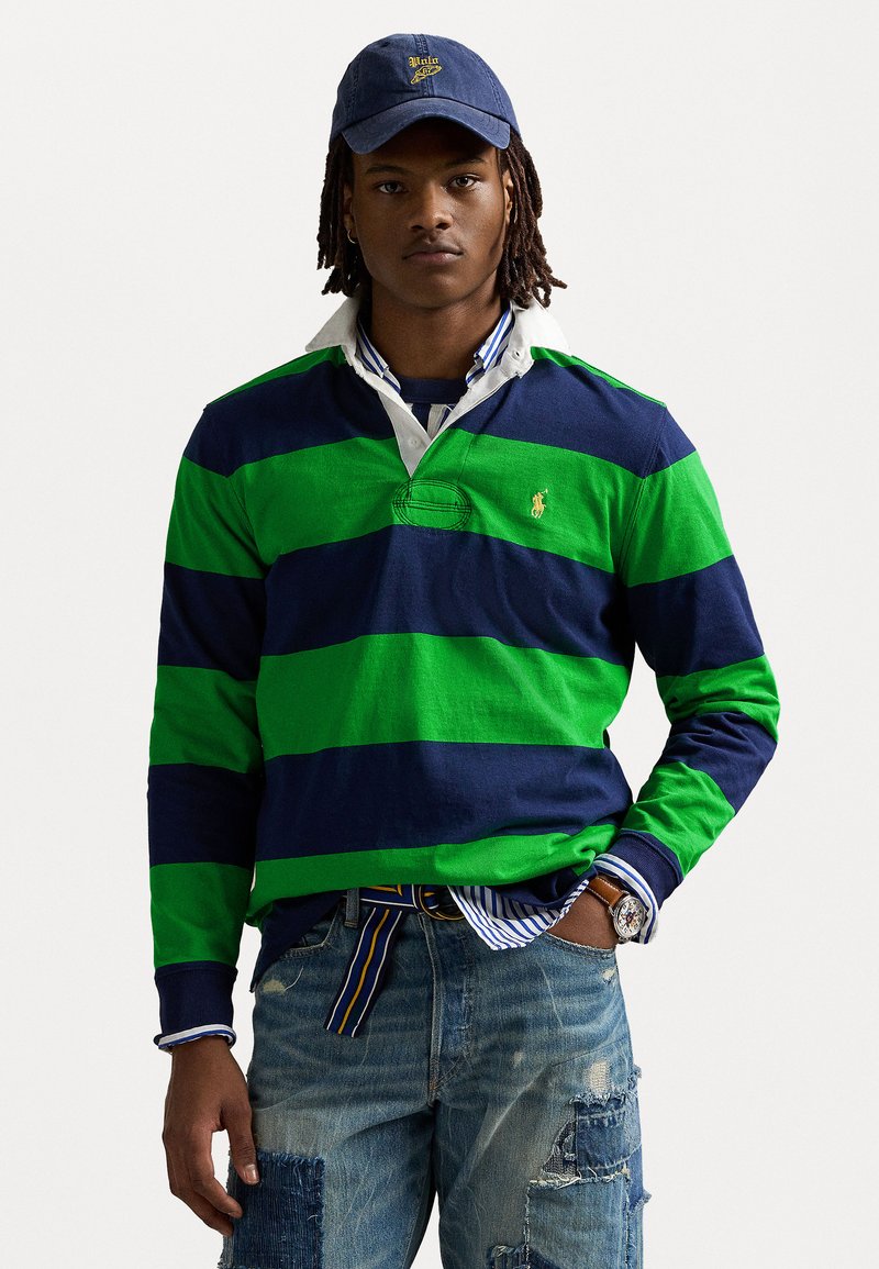 Green and navy striped rugby shirt with a collar, paired with distressed blue jeans. A navy cap with logo completes the outfit.