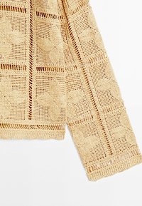 Beige haakstof met vierkante en bloemmotieven, met gedetailleerde mouw- en lichaamgedeelten van een gebreid kledingstuk.