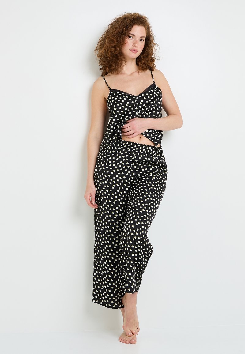 Ensemble de pyjama noir avec des pois blancs, comprenant un haut sans manches et un pantalon large. Fabriqué dans un tissu doux avec une coupe décontractée et des bretelles ajustables.