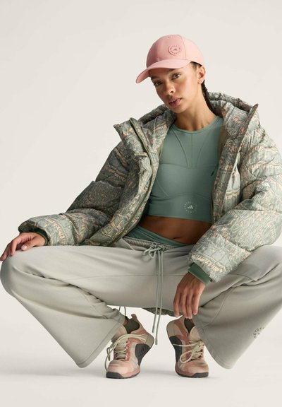 Gewatteerde jas in het groen met een gestructureerd patroon, gecombineerd met een lichtgroen cropped top, grijze losse broek en atletiekschoenen in rozetinten.