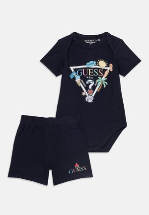 Ensemble pour bébé composé d'un body et d'un short bleu marine avec des logos Guess colorés sur le thème de l'été, des graphiques de soleil, de palmier, de glace et de pastèque.