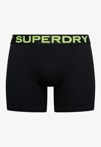 Boxer noir pour homme avec une large ceinture noire, portant un grand texte vert « SUPERDRY » à l'avant.