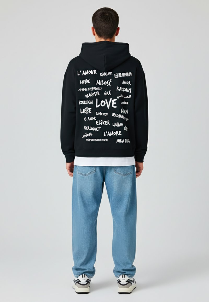 Felpa nera con scritte bianche che riportano "LOVE" e varie traduzioni, abbinata a jeans azzurri e sneakers.
