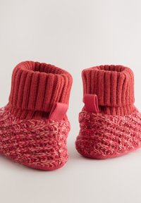 Dziane kapcie w różnych odcieniach czerwieni, z żebrowanym mankietem, tkaną teksturą i pętelką z tyłu ułatwiającą zakładanie.