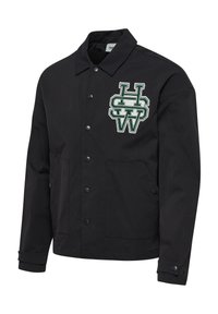 Svart jacka i tyg med krage, tryckknappar och två framfickor. Har en broderad logotyp i grön och vit på bröstet.