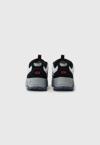 Pair of black and white sneakers with thick gray soles, viewed from the back, featuring a red logo and red pull tabs on a white background.