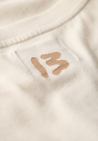 Tessuto di cotone beige con un grande numero "13" dipinto in marrone, caratterizzato da una texture che appare leggermente in rilievo rispetto allo sfondo liscio.