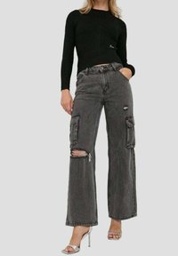 Schwarzes, geripptes Langarmshirt kombiniert mit grauen, weit geschnittenen Cargo-Jeans mit abgewetzten Knien und Seitentaschen. Metallische High Heels runden den Look ab.