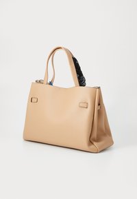 Beige kožená taška na rameno s dvěma uchy, zdobená černým vzorovaným šátkem na vrchu, hladkým povrchem a strukturovaným tvarem.