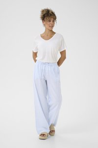 T-shirt bianca a V abbinata a pantaloni larghi a righe blu chiaro con vita elastica e tasche laterali, indossati con sandali con zeppa in tonalità neutre.