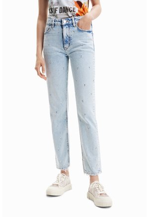 Jeans de mezclilla azul claro con corte recto, adornados con pequeños remaches brillantes, dobladillo deshilachado y textura desgastada, combinados con zapatillas blancas.