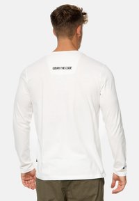 Weißes Langarmhemd mit glatter Textur, das auf dem oberen Rücken mit schwarzem Drucktext "WEAR THE CODE" versehen ist und seitliche Schlitze hat.