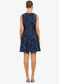 Vestito nero con ricami floreali blu, design senza maniche, corpino aderente, gonna svasata e chiusura con cerniera sul retro. Le scarpe con tacco completano il look.