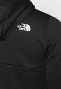 Giacca nera con cappuccio caratterizzata da un tessuto testurizzato, dettagli a coste e il logo bianco di The North Face sul lato sinistro superiore.