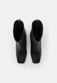 Pár černých kožených kotníkových bot se čtveratými špičkami a zadními zipy, pohled shora na bílém pozadí.