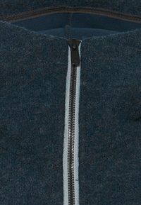 Tmavomodrý plsťový výrobok so zipsom, ktorý má výrazný strieborný zips s svetlomodrým lemom na šve a vyznačuje sa textúrovaným povrchom.