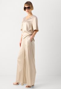 Beige satin top with short sleeves and a V-neck, paired with wide-leg beige satin pants featuring side pockets. Model wears oversized sunglasses.