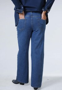 Blauwe denim jeans met een brede pasvorm, voorzien van twee achterzakken en gedetailleerde stiksels. De stof heeft een gladde textuur.