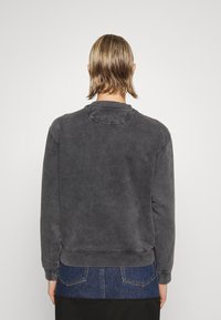 Sudadera gris con una textura deslavada, cuello redondo y puños acanalados. La parte trasera presenta un diseño simple, destacando el corte holgado.