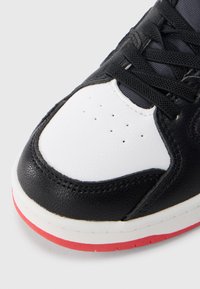 Μαύρο δερμάτινο αθλητικό πα πούτσι με λευκή δερμάτινη μύτη, κόκκινη λαστιχένια σόλα και μαύρα κορδόνια. Διαθέτει οπές για αναπνοή.