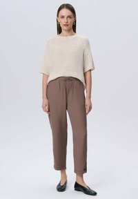 Kremowy sweter dzianinowy z krótkimi rękawami, zestawiony z luźnymi brązowymi spodniami i czarnymi balerinami. Prosty design, miękka tekstura i neutralne kolory.