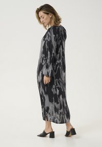 Black and gray long dress with a flowing design, featuring a subtle abstract pattern and long sleeves. Slit on both sides. Black block-heeled shoes.
