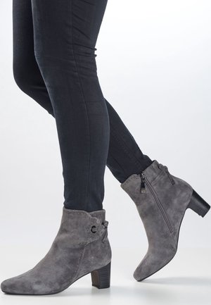 Botas de tobillo de ante gris con tacón de bloque, con tachuelas decorativas, un cierre de cremallera lateral y un detalle de lazo en el eje.