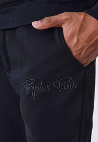 Zwarte sweatpants met een strakke tailleband, zijzakken en subtiele geborduurde tekst "Project x Paris" op het linker zakgebied.