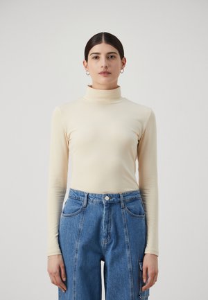 Beige polo-genser laget av stretchstoff, kombinert med blå høyt liv denimbukser med store sidelommer og en avslappet passform.