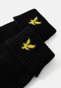 Svarte strikkede hansker har en ribbet mansjett og en brodert gul fugledesign på toppen. Den teksturerte stoffer gir visuell interesse.