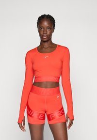 Red long-sleeve crop top and matching shorts, featuring a "NIKE PRO" waistband and logo, made from stretchy material. Smooth texture.