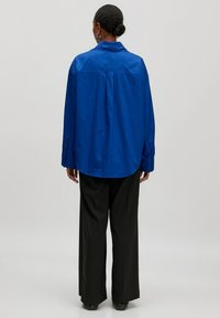 Blauwe oversized shirt gemaakt van gladde stof, met een kraag en knoopmanchetten, gecombineerd met losse zwarte broek voor een relaxte pasvorm.