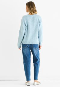 Light blue knitted sweater with a relaxed fit, ribbed hem, and dropped shoulders, paired with high-waisted blue jeans and silver flats.