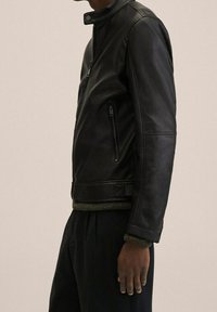 Zwarte leren jas met een opstaande kraag, zijritszak en geribbelde groene gebreide details aan de zoom en manchetten.