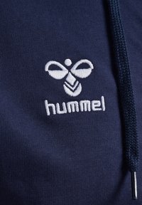 Navy hoodie featuring white embroidered logo with a bee design and the brand name "hummel" below it. Smooth texture with drawstring.
