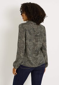 Blusa de manga larga en negro y crema con un patrón de puntos en espiral, con cuello entallado y cierre de botones, fabricada con tela ligera.