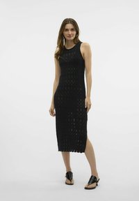 Černé pletené bezrukávové šaty s přiléhavým střihem, otevřeným vzorem a délkou do poloviny lýtek se bočním rozparkem, doplněné černými sandály.