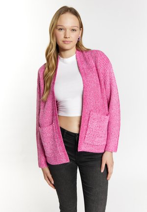 Roze gebreide cardigan met een textuurpatroon, open voorkant en voorzakken. Gecombineerd met een witte top en zwarte denim, wat een casual look laat zien.