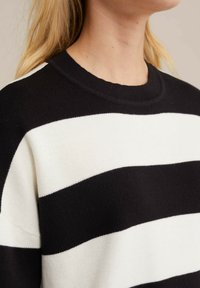 Ribakujund, millel on paksud mustad ja valged horisontaalsed triibud, ümar kaelus ja pehme kudumise tekstuur. Suumvaade kaeluse piirkonnale.