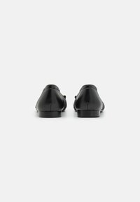 Scarpe slip-on in pelle nera con una texture liscia e tacco basso, dotate di punta arrotondata e design minimalista.