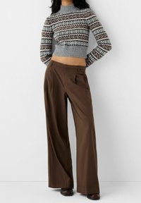 Grå mönstrad stickad tröja med hög krage, kombinerad med bruna vida byxor och svarta skor. Mjuk textur, avslappnad passform.