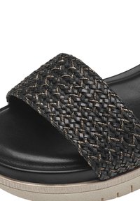 Svart sandal med en bred vävd rem som har metalliska detaljer, dämpad sula och strukturerad yta. Designen är platt med en subtil plattform.