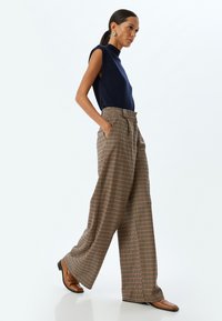 Marineblauw mouwloos topje gecombineerd met wijde geruite broek in bruin, oranje en groen. Bruine schoenen maken de outfit compleet.