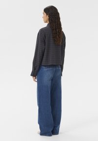 Abgeschnittetes, dunkelgraues kariertes Hemd mit langen Ärmeln, kombiniert mit hoch taillierten, weit geschnittenen blauen Jeans. Glatte Stofftextur sichtbar.