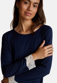 Top a maniche lunghe blu navy con scollatura tonda e pizzo bianco ai polsini. Tessuto morbido e liscio con una vestibilità rilassata e dettagli minimi.